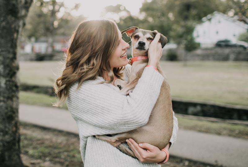smiling woman carring a dog near tree